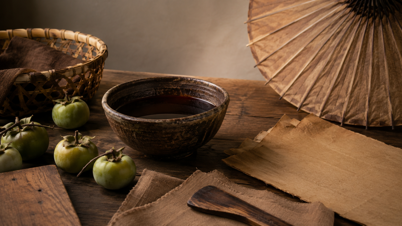 Traditional ceramic tea bowl with green persimmons and a paper umbrella on a rustic wooden table.