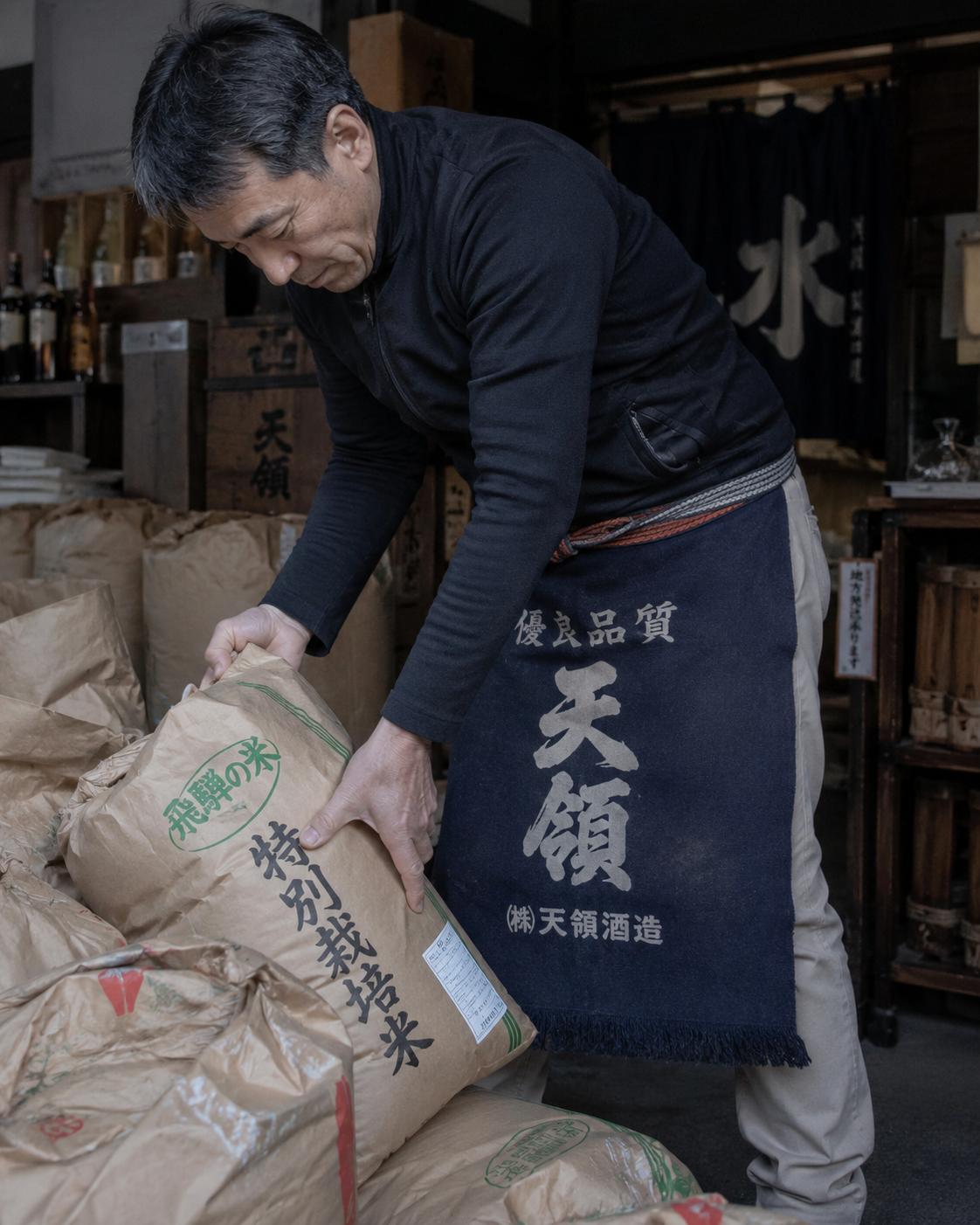 A Japanese worker lifts a heavy sack of rice at a traditional sake brewery in Japan.