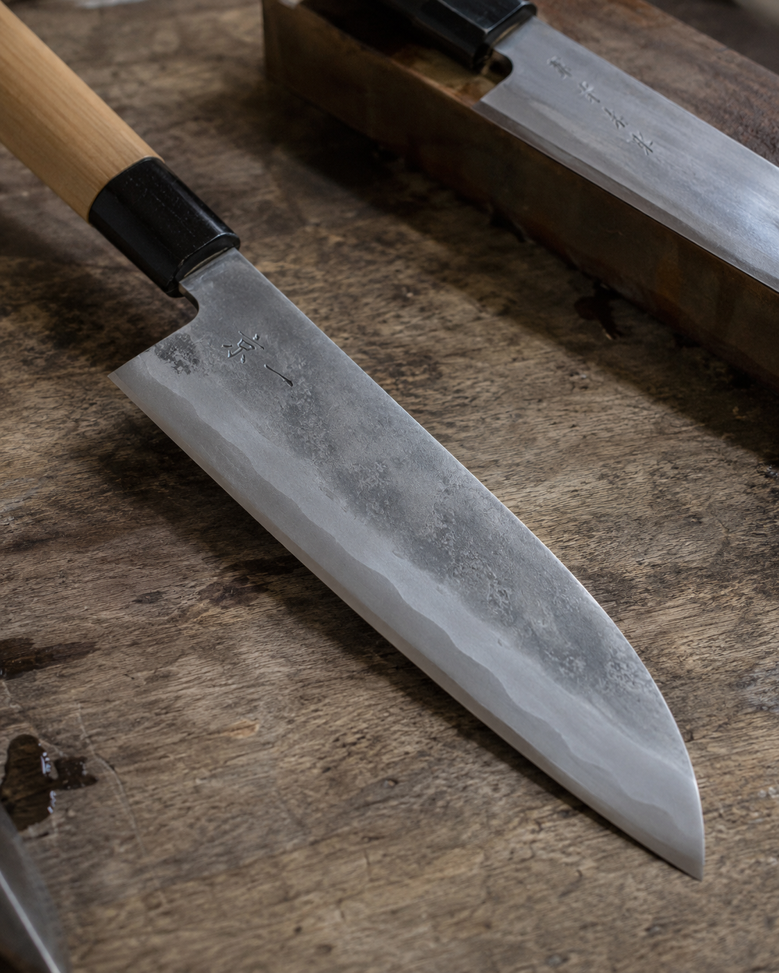 Hand-forged Japanese Santoku kitchen knife with carbon steel blade on a wooden cutting board.